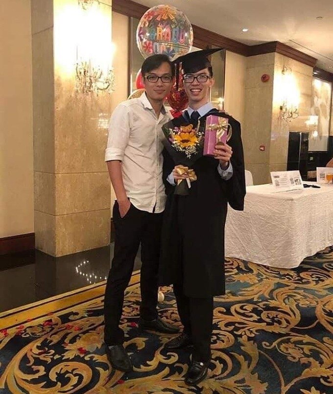 caption: Nguyết Viết Phúc (áo trắng) chụp ảnh cùng em trai tại lễ tốt nghiệp master của em trai tại Singapore.