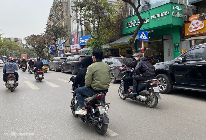 Hai người điều khiển xe máy điện không đội mũ bảo hiểm di chuyển trên đường Đào Tấn, quận Ba Đình, trưa 20/3. Ảnh: Quỳnh Nguyễn