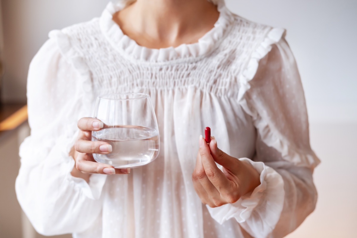 6 thành phần cần lưu ý khi dùng vitamin tổng hợp- Ảnh 2. Người phụ nữ mặc áo trắng cầm một viên thuốc màu đỏ trong một tay và tay kia cầm ly nước