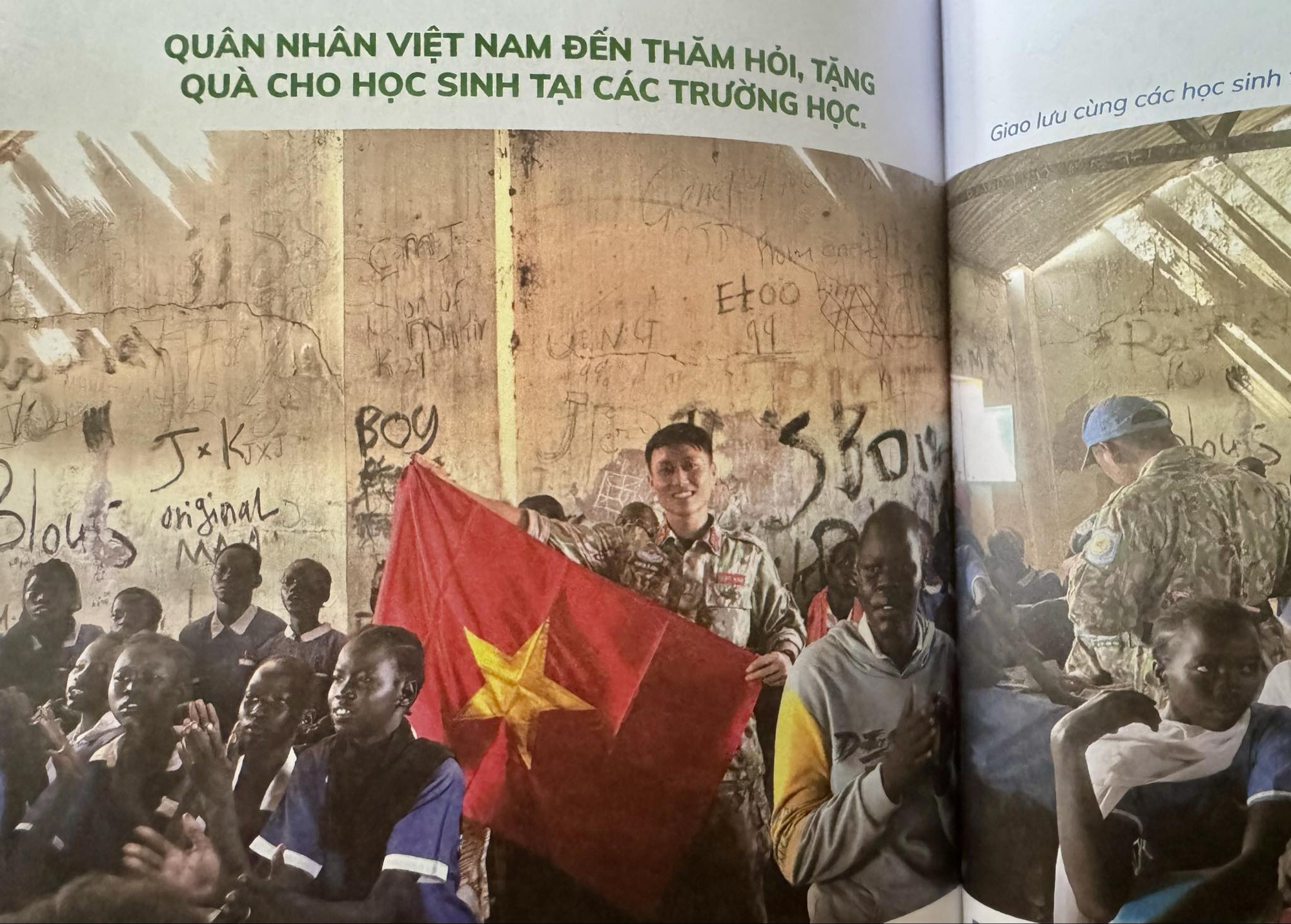 Nếu hòa bình là một hạt giống, hãy đem nó gieo vào lòng trẻ thơ- Ảnh 2. Hình ảnh anh Công bên lá cờ Việt Nam tại trường Prat khi anh đến thăm hỏi, tặng quà cho các em học sinh ở đây - Ảnh: chụp từ sách
