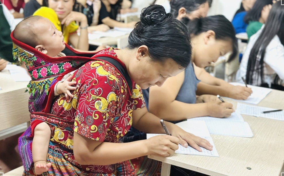 Chồng địu con để vợ đi học lớp xóa mù chữ- Ảnh 1. Chồng địu con để vợ đi học lớp xóa mù chữ- Ảnh 1.